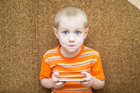 Little boy sitting on the couch with surprised eyes and holding a smartphone