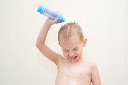 little boy in the bathroom on a white background pour it on his head with a bottle of waterの写真素材