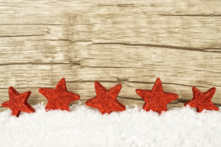Five red twinkling stars in the snow with wooden background