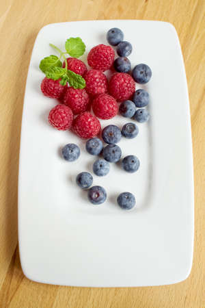 Blueberries and raspberries on a white plateの写真素材