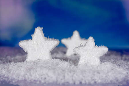 Christmas decoration from three snow stars standing against blue background on snowの写真素材