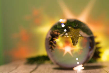 A glass sphere with a golden star and pine branch inside and bright stars in green background, selected focusの写真素材