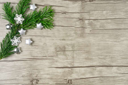 Branch of a fir tree with little snowcrystals and silver stars on wooden background with copy spaceの写真素材