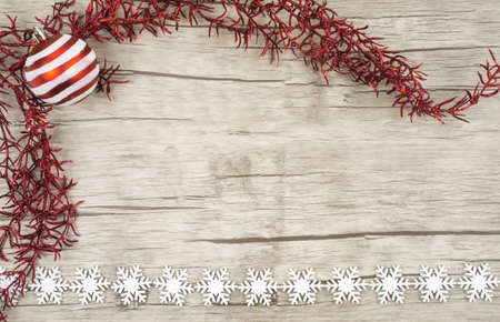 Red glittering twig with a red and white striped Christmas ball on wooden background with decorative snowcrystals of wood at the bottom pictured copyspaceの写真素材