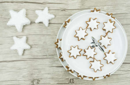 A white plate with Christmas biscuits, cinnamon stars with frosting on wooden background, in the left corner are three stars with snowの写真素材