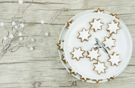A white plate with Christmas biscuits, cinnamon stars with frosting on wooden background, on the left is a decorative branch with white balls, copyspaceの写真素材