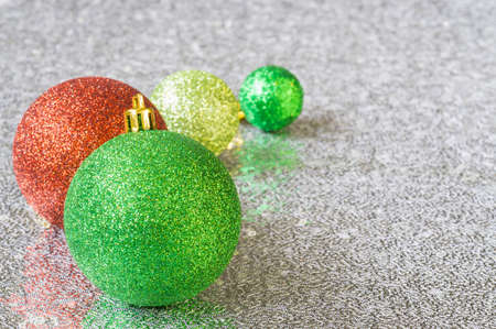 Four glittering Christmas tree balls in green, red and golden color on silver fabric with sequins, copyspaceの写真素材