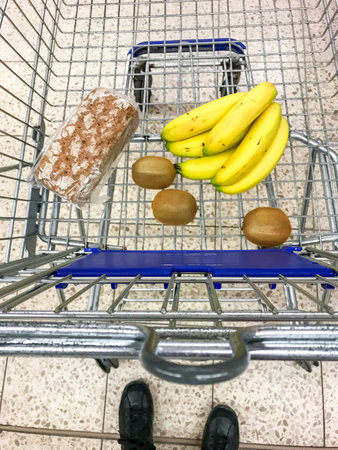 Shopping trolley with bananas, kiwi fruit and breadの写真素材