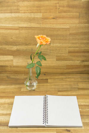 Opened notebook with orange rose and squared lines, wooden backgroundの写真素材