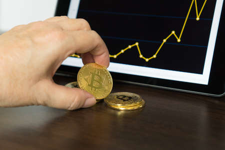 Tablet with a chart and a hand with bitcoinsの写真素材