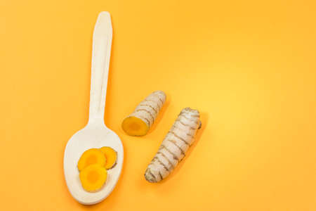 Sliced ??turmeric root on a wooden spoon, orange backgroundの写真素材