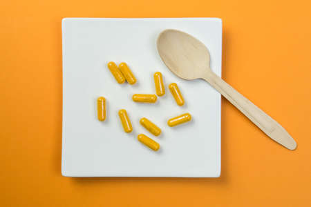 Yellow vitamin pills with a wooden spoon on orange backgroundの写真素材
