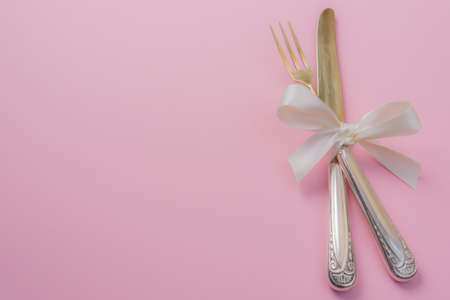 Silver fork and knife with white ribbon on pink backgroundの写真素材