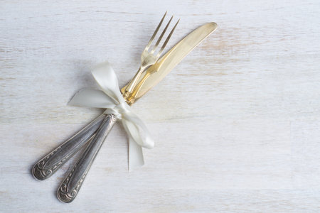 Silverware with white ribbon on white wooden background