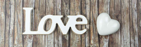 The word love in wooden letters with a white heart beside, wooden backgroundの写真素材