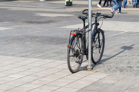 a black bicycle tethered to a sign, in the background you can see the legs of peopleの写真素材