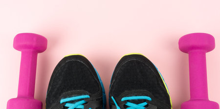 Two pink dumbbells and shoe tips of sneakers on pink background, banner