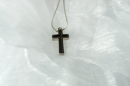 A silver cross with black inlet on a delicate white organza fabric