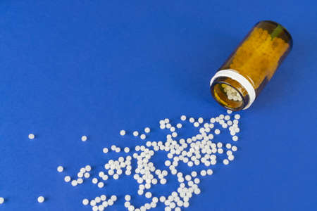 An overturned glass with homeopathic globules spread over the blue backgroundの写真素材