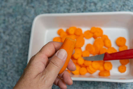 Woman holds a piece of carrot in her hand, in the background you can see a white bowl of freshly cut carrotsの写真素材