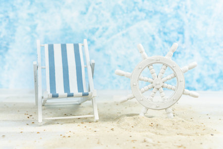 Maritime  background with sand, an old white ships wheel and a blue and white striped beach chair