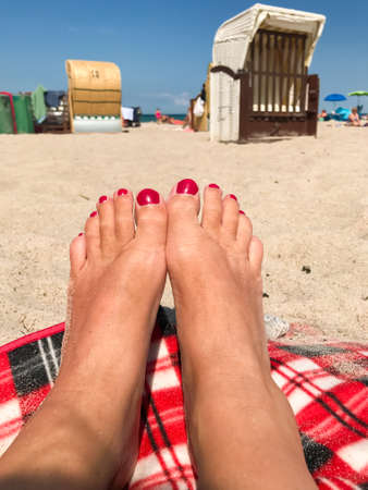 Woman feet with red nail polish at the beach, in the background beach chairs and blue skyの写真素材
