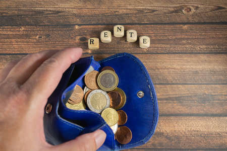 Hand holds a blue wallet with euro coins, wood background with the german word for pensionの写真素材