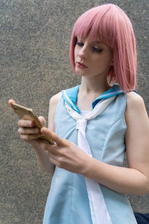 Young woman with pink hair and blue dress is typing on her cellphoneの写真素材