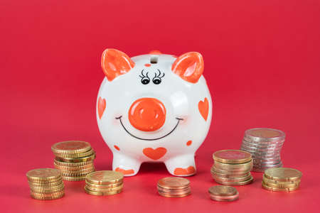 Cute piggy bank with red hearts, many coins and red background, copy spaceの写真素材