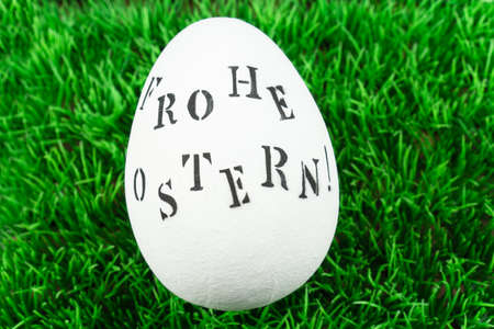 A white easter egg with the german words for happy easter in the grassの写真素材