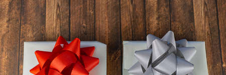 Two white-wrapped gifts on a wooden table, one with a red bow and the other with a silver bowの写真素材