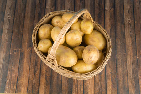 A wicker basket with fresh potatoes on a wooden table, view from aboveの写真素材