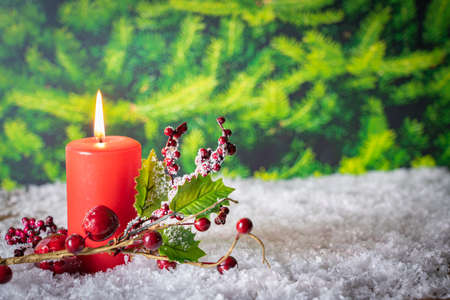 Burning red candle with a branch in the snow, copy spaceの写真素材