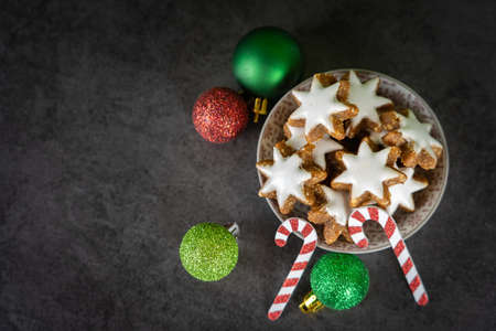 A cup with Christmas biscuits on black background and green and red Christmas baublesの写真素材