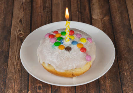 Delicious small birthday cake with one burning candle on wooden backgroundの写真素材