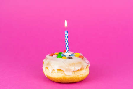 Delicious birthday cake with a burning candle, pink background with copy spaceの写真素材