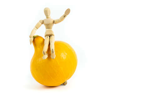 Yellow pumpkin with a small wooden figure sitting on it and waving, white background, copy spaceの写真素材