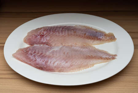Two fillets of freshly caught redfish on a white plate, wooden table as a backgroundの写真素材