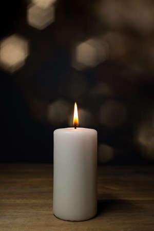 A white burning candle on a wooden table, lensflares background and copy spaceの写真素材