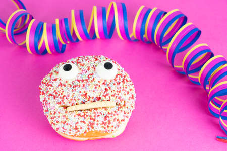 Delicious cake with a funny face, pink background and streamersの写真素材