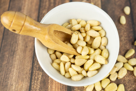 White bowl with wooden spoon and many pie nuts, wooden background and top viewの写真素材