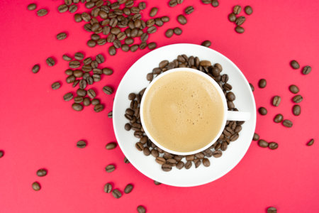 A cup of creamy coffee with roasted coffee beans, red background and copy spaceの写真素材