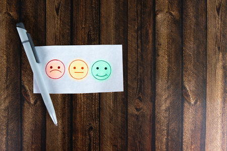 Three smiley faces to tick, a sad, a neutral and a laughing smiley, wooden background and a penの写真素材