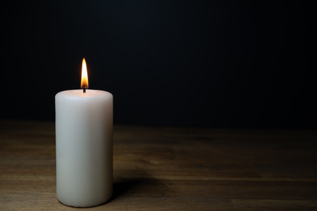 A white burning candle on a wooden table, dark background and copy spaceの写真素材