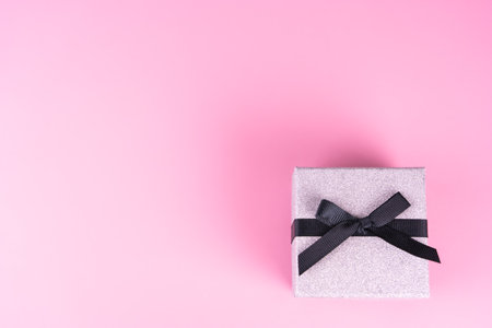 Small silver gift package with black bow, pink background, copy spaceの写真素材