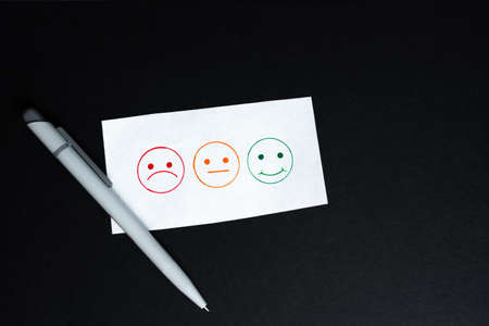 Three smiley faces to tick, a sad, a neutral and a laughing smiley, black background and a penの写真素材