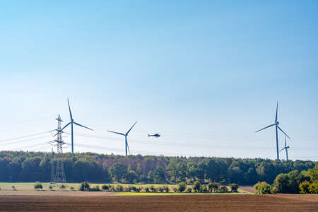 Helicopter flies between wind turbines and overhead power linesの写真素材