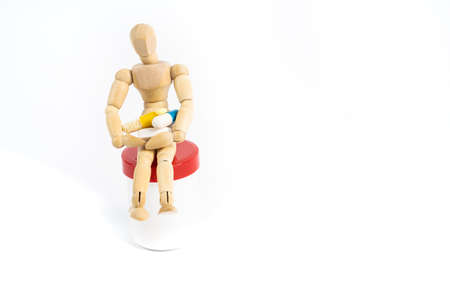 Small wooden figure sits on a pill box and holds various tablets in his arms, white background and copy spaceの写真素材