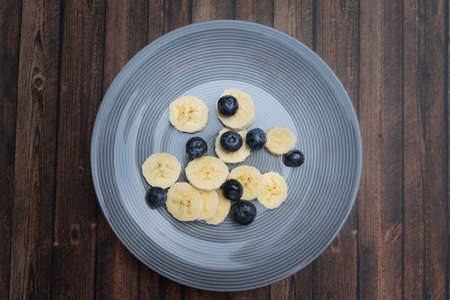 Sliced ââbanana and blueberries on a plate, wooden background and view from aboveの写真素材