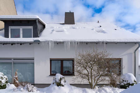 Snow-covered house with icicles on the gutterの写真素材